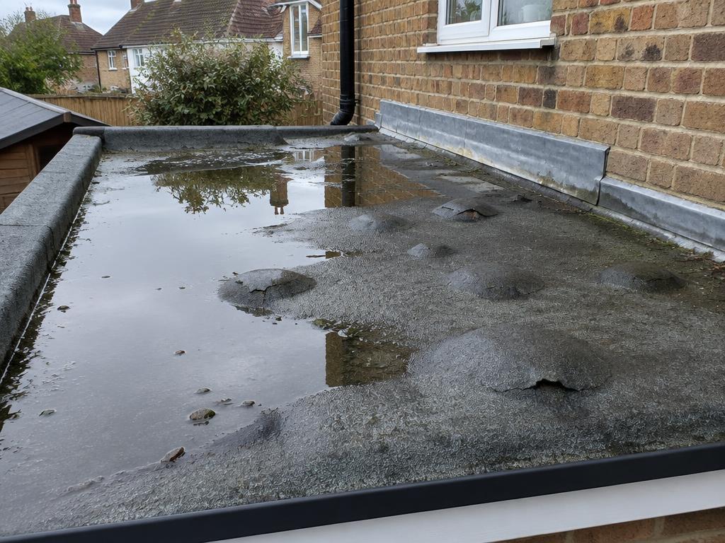 Illustrative example: blistered felt flat roof with standing water and a worn wall abutment flashing