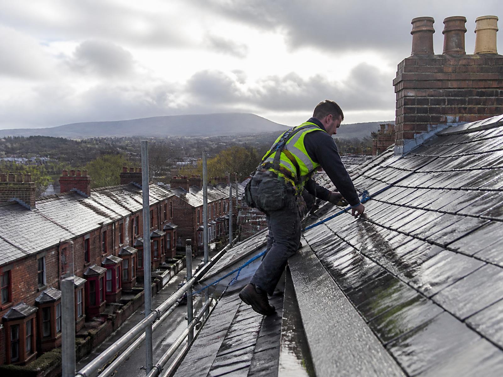 Roofer working on a wet natural slate roof above a Victorian terraced street in Carlisle, with the Cumbrian fells behind
